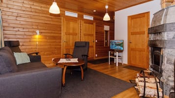 A cozy living room with wooden walls, a fireplace, a sofa, a table, and two chairs.