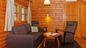 A log cabin interior with a sofa, two armchairs, a small table, and a hanging light fixture.