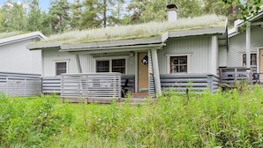 Een chalet met een schuin dak begroeid met begroeiing, een houten veranda en een zichtbare schoorsteen.