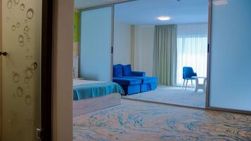 Una habitación de hotel con una cama, un sofá azul, una silla y un amplio ventanal corredizo.