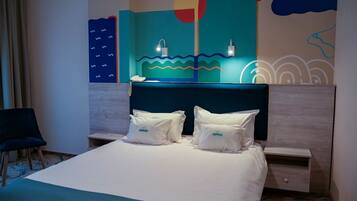 Habitación de hotel con cama, dos almohadas, mesita de noche, silla y una pared decorada con arte abstracto.