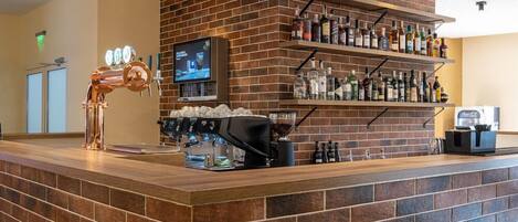 A bar area with a brick wall, shelves with bottles, a coffee machine, and a television screen.