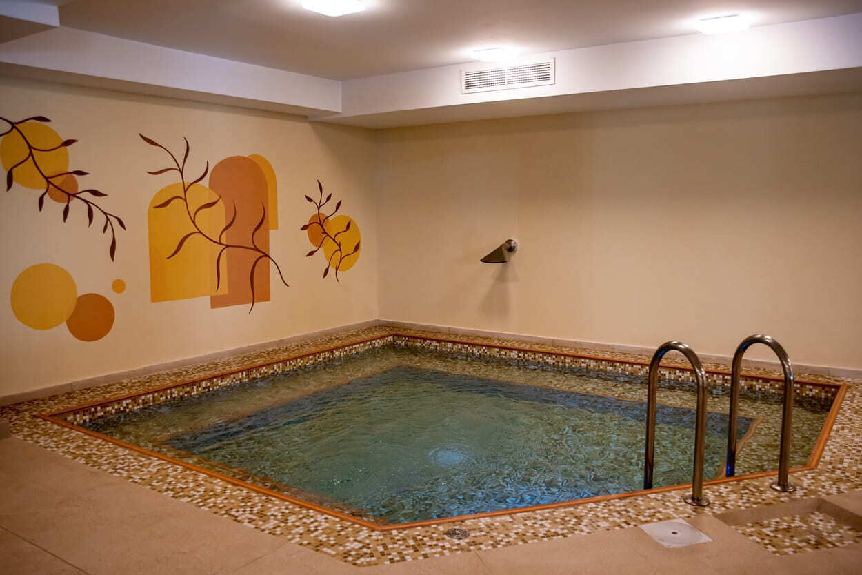 Una piscina con borde de azulejos, una pared con arte abstracto y un respiradero en el techo.
