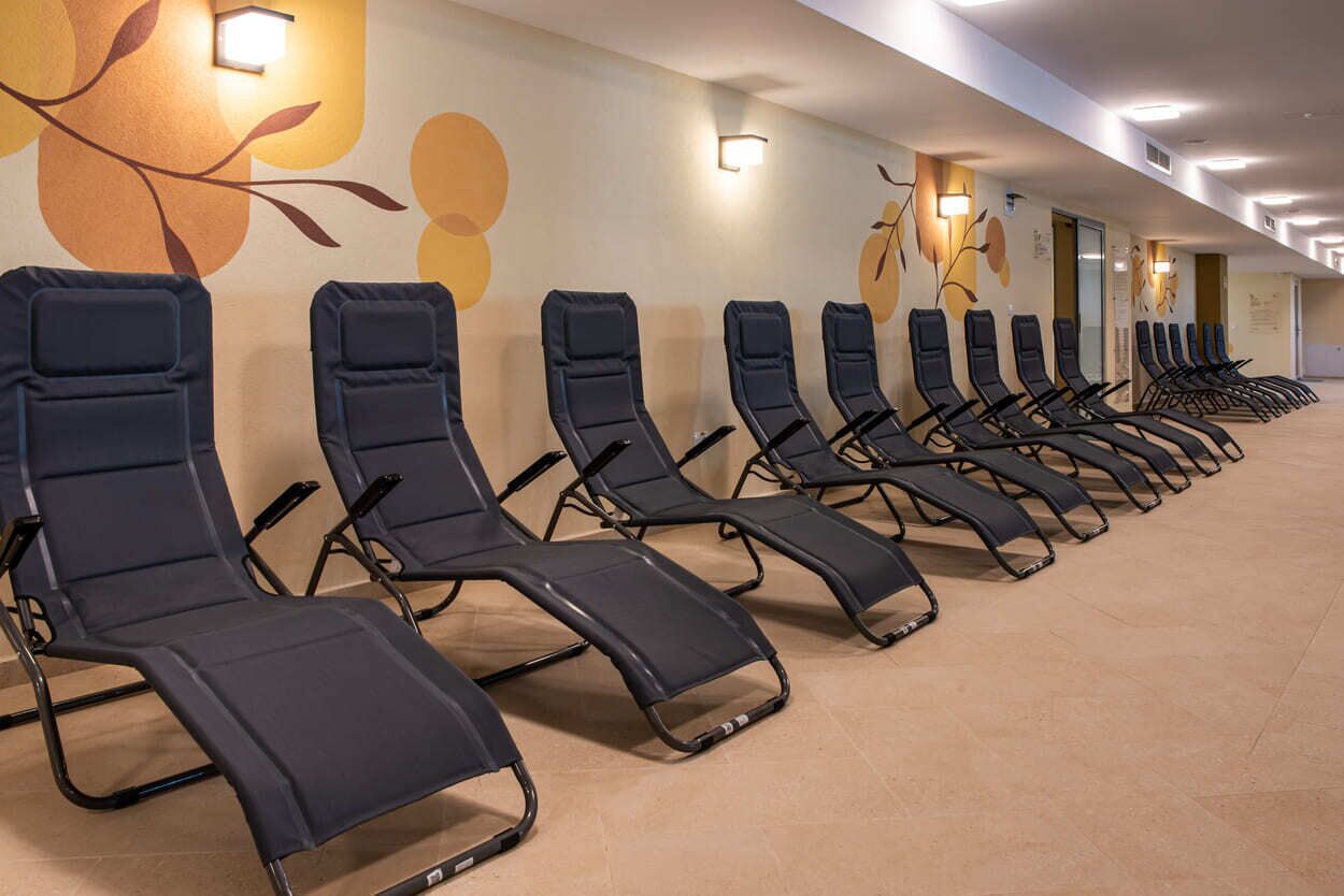 A row of reclining chairs in a hotel lobby with a floral wall mural and wall-mounted lights.