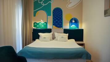 Ein Hotelzimmer mit Bett, zwei Nachttischen, einem Sessel und einer Wand mit abstrakter Kunst.