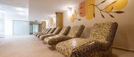 A row of mosaic-patterned lounge chairs in a spacious, well-lit hallway with a modern design and a wall mural.