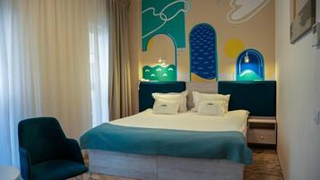 A hotel room with a bed, a chair, a nightstand, and a wall with abstract art.