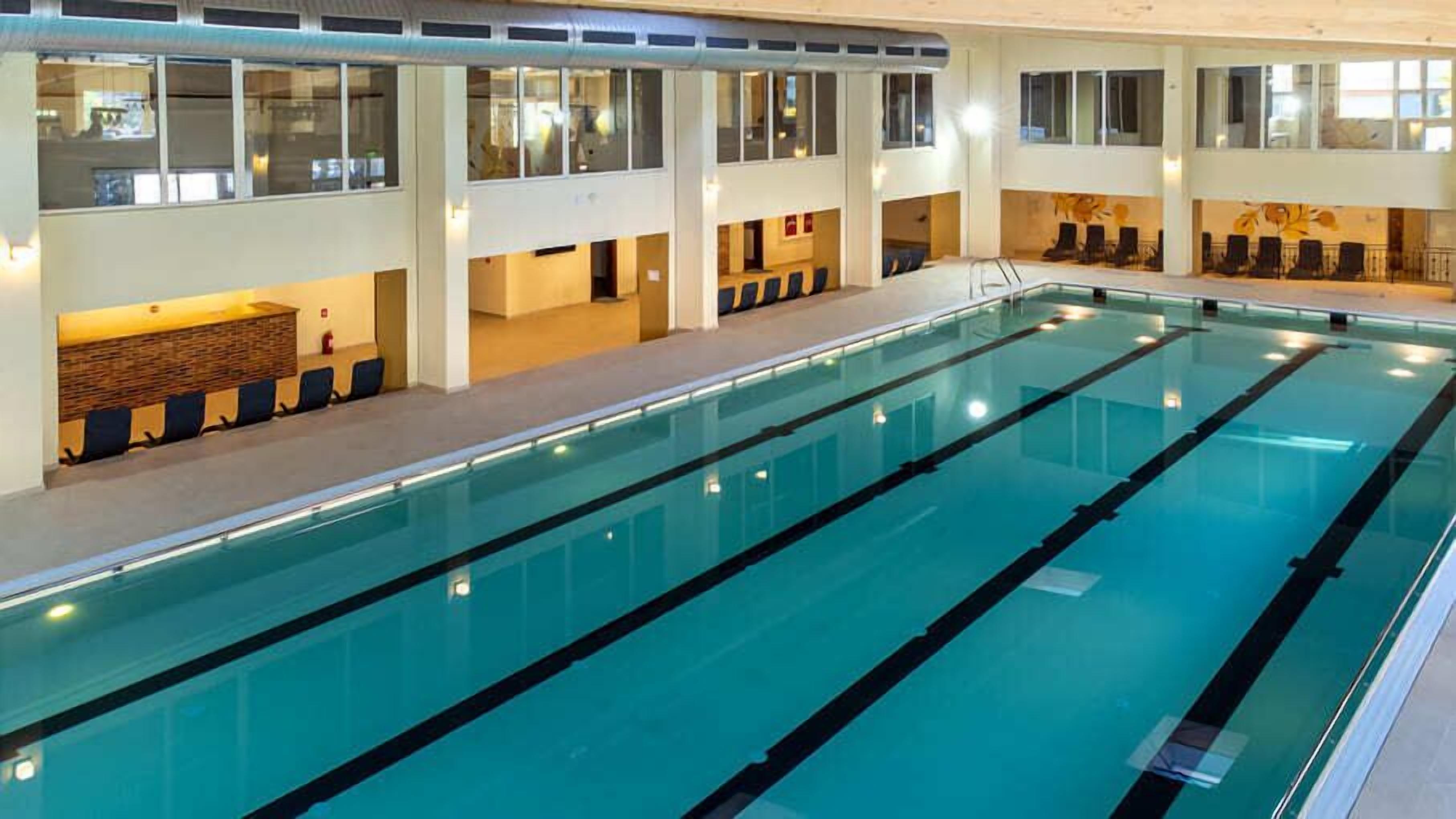 A large indoor swimming pool with multiple lanes, seating areas, and a high ceiling with windows.