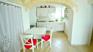 Una cucina con mobili bianchi, un tavolo bianco e sedie con cuscini rossi.