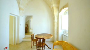 Zona pranzo con un tavolo rotondo e sedie, una sedia in vimini e un arco in pietra.