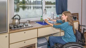 A wheelchair-accessible kitchen with a window view of a lake, a kettle, and a sink. - Boats & Yachts at Zehdenick Harbor by Kuhnle‑Tours  (Zehdenick)