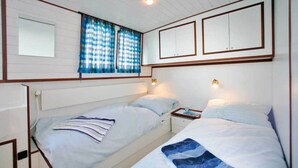 A bedroom with two beds, a nightstand with a lamp, a window with curtains, and a mirror. - Boats & Yachts at Zehdenick Harbor by Kuhnle‑Tours  (Zehdenick)