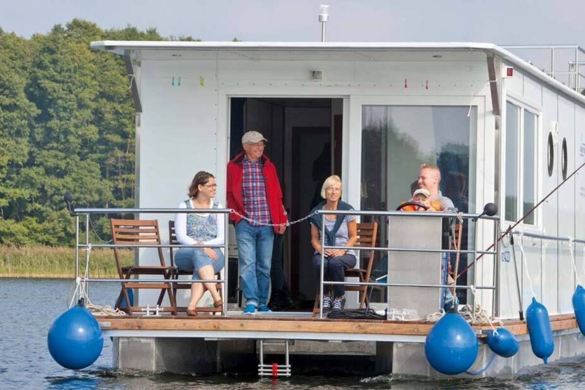 A houseboat with a deck, seating, and a small enclosed area with windows.