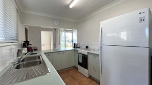 A kitchen with a white refrigerator, a sink, cabinets, a stove, and a window with curtains.