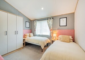 A bedroom with two beds, a wardrobe, a window with curtains, and a bedside lamp. - Hot Tub Lodge 3 Pet Friendly (Kirkcudbright)