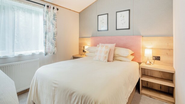 Un dormitorio con cama, mesitas de noche, una ventana con cortinas e imágenes enmarcadas en la pared.