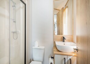 Un baño con cabina de ducha de vidrio, inodoro, lavamanos con espejo y muebles de madera.