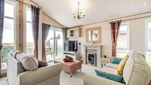 A living room with a fireplace, a television, and two sofas. - Country and modern cladded lodge with sea views. (Kirkcudbright)