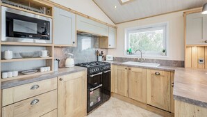 A modern kitchen with a built-in microwave, stove, and oven, wooden cabinets, and a window with a view. - Country and modern cladded lodge with sea views. (Kirkcudbright)