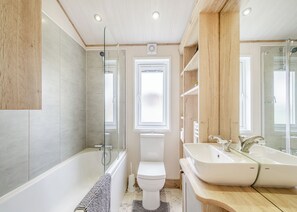 Een moderne badkamer met een badkuip, toilet en twee wasbakken.