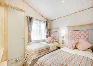 A bedroom with two beds, a wardrobe, a window with curtains, and a headboard with a light fixture.