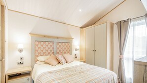 Quarto com cama, mesas de cabeceira, guarda-roupa e janela com cortinas.