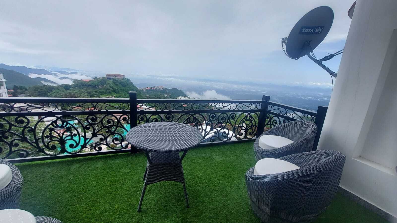 A balcony with artificial grass, a table, two wicker chairs, a decorative fence, and a satellite dish.