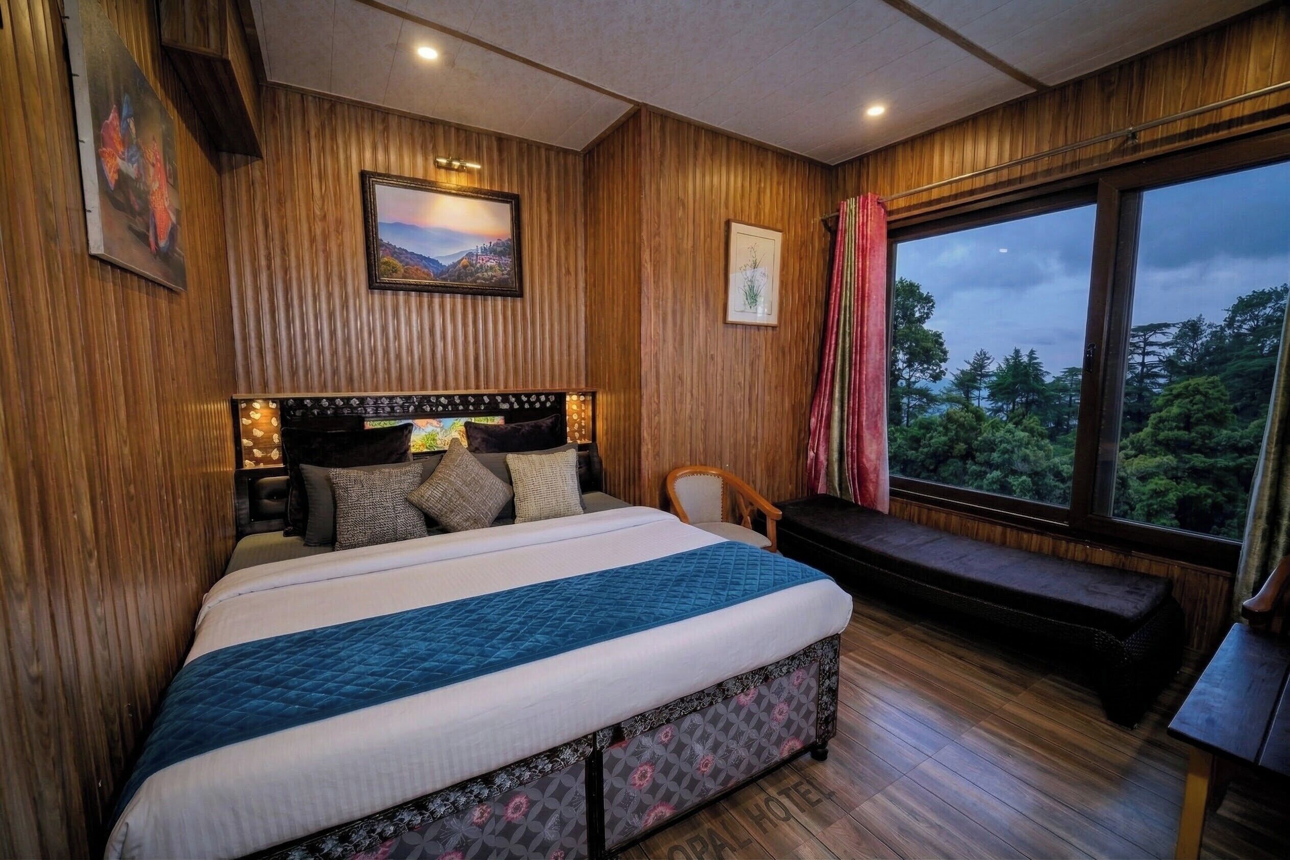 Un dormitorio con una cama grande, un banco, una ventana con vistas a árboles y paredes de madera.