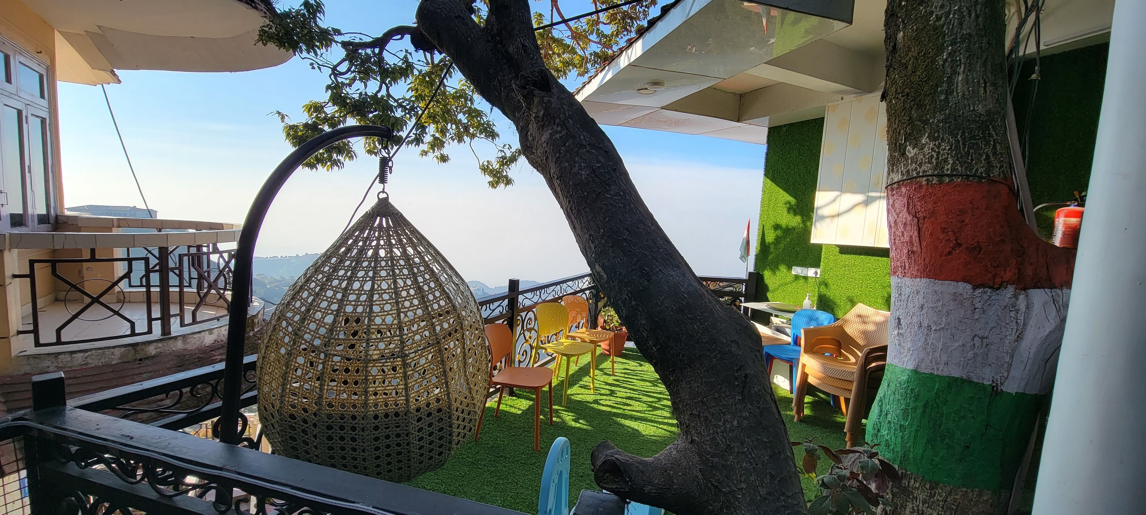 A balcony with a hanging wicker chair, a tree, and a view of the cityscape.