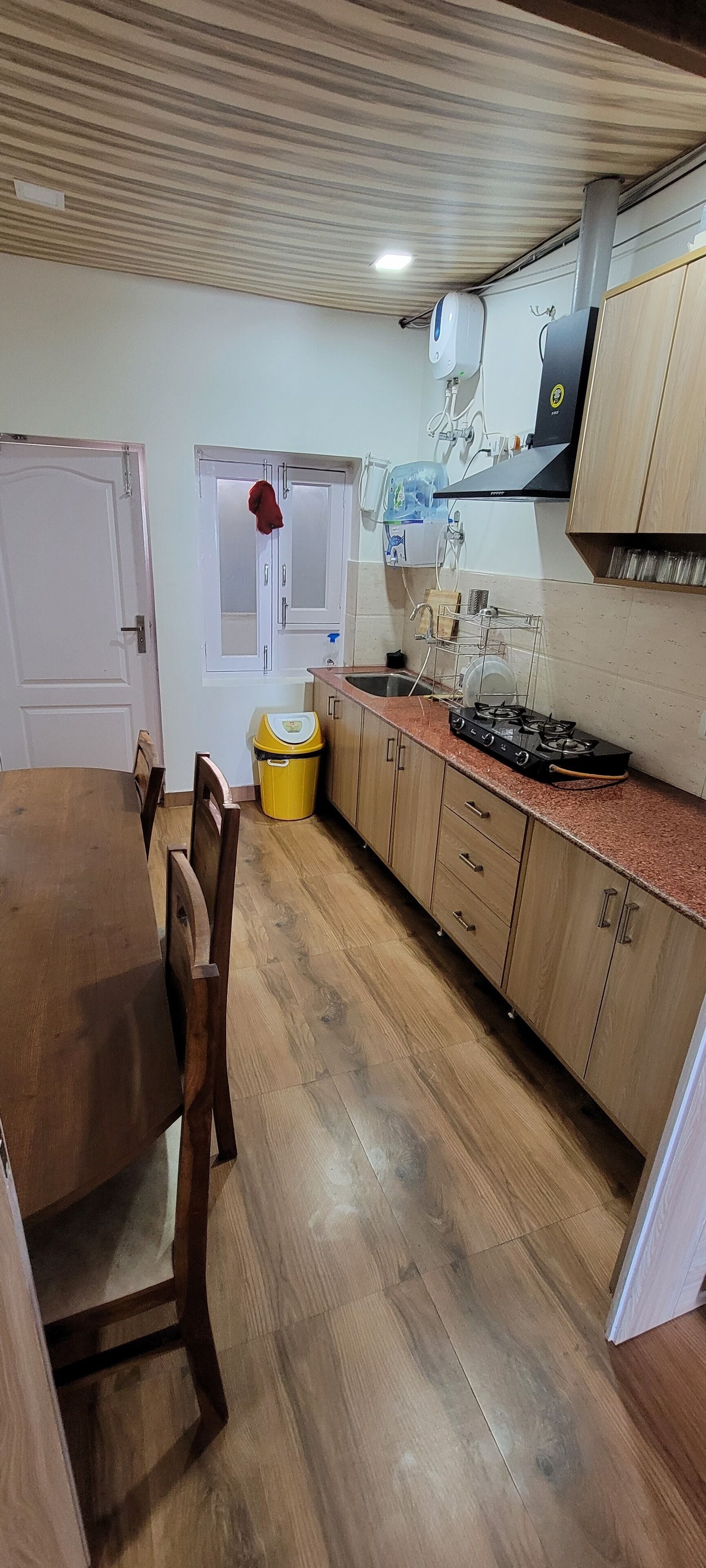 A kitchen with wooden cabinets, a gas stove, a sink, and a trash bin.