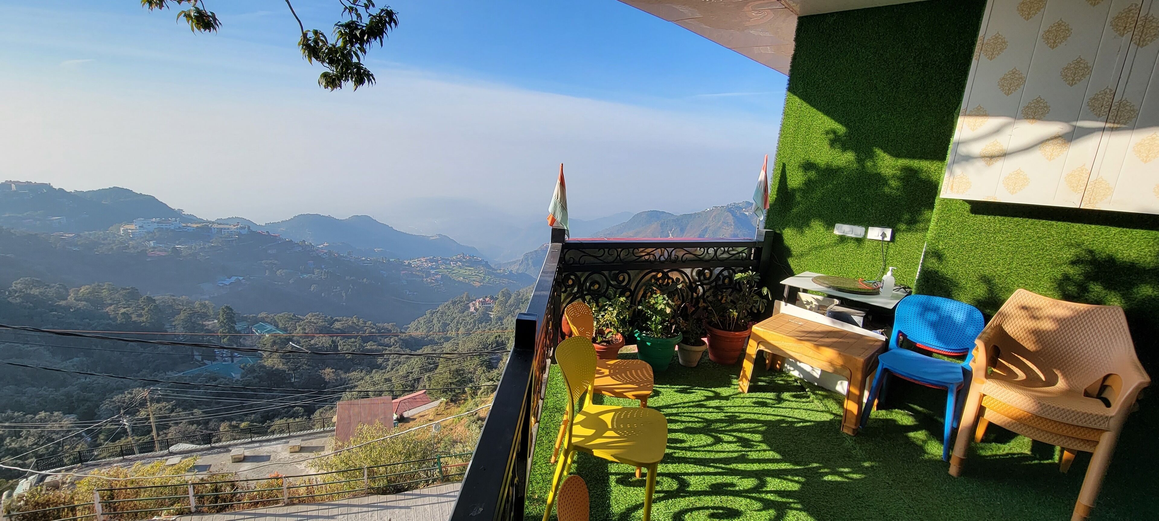 A balcony with a view of mountains, a flag, and outdoor furniture.