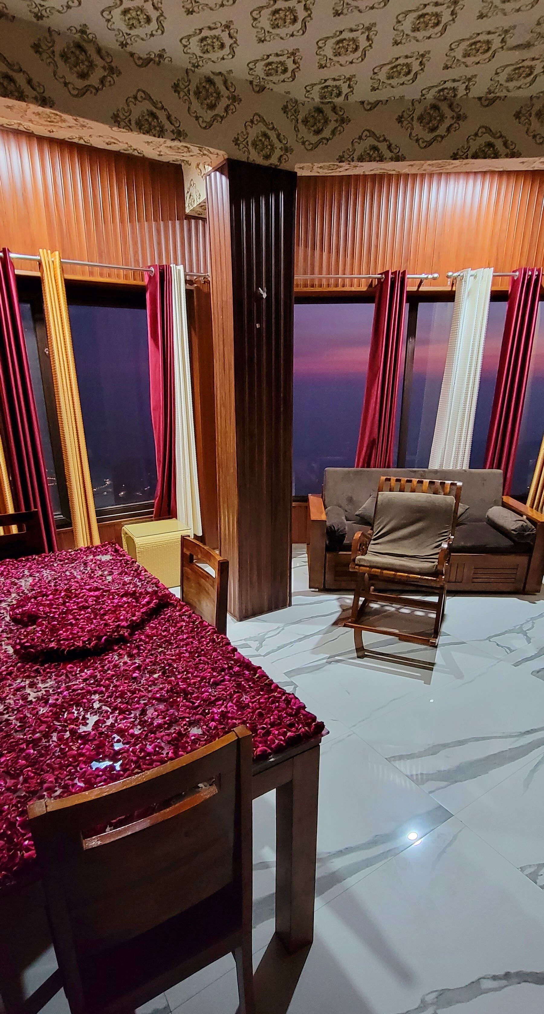 A room with a bed covered in rose petals, a wooden chair, a sofa, and a table.