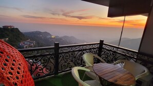 A balcony with wicker chairs and a table, overlooking a mountainous landscape during sunset. - Casa Arhan Luxury Mussoorie Homestay (Dehradun)