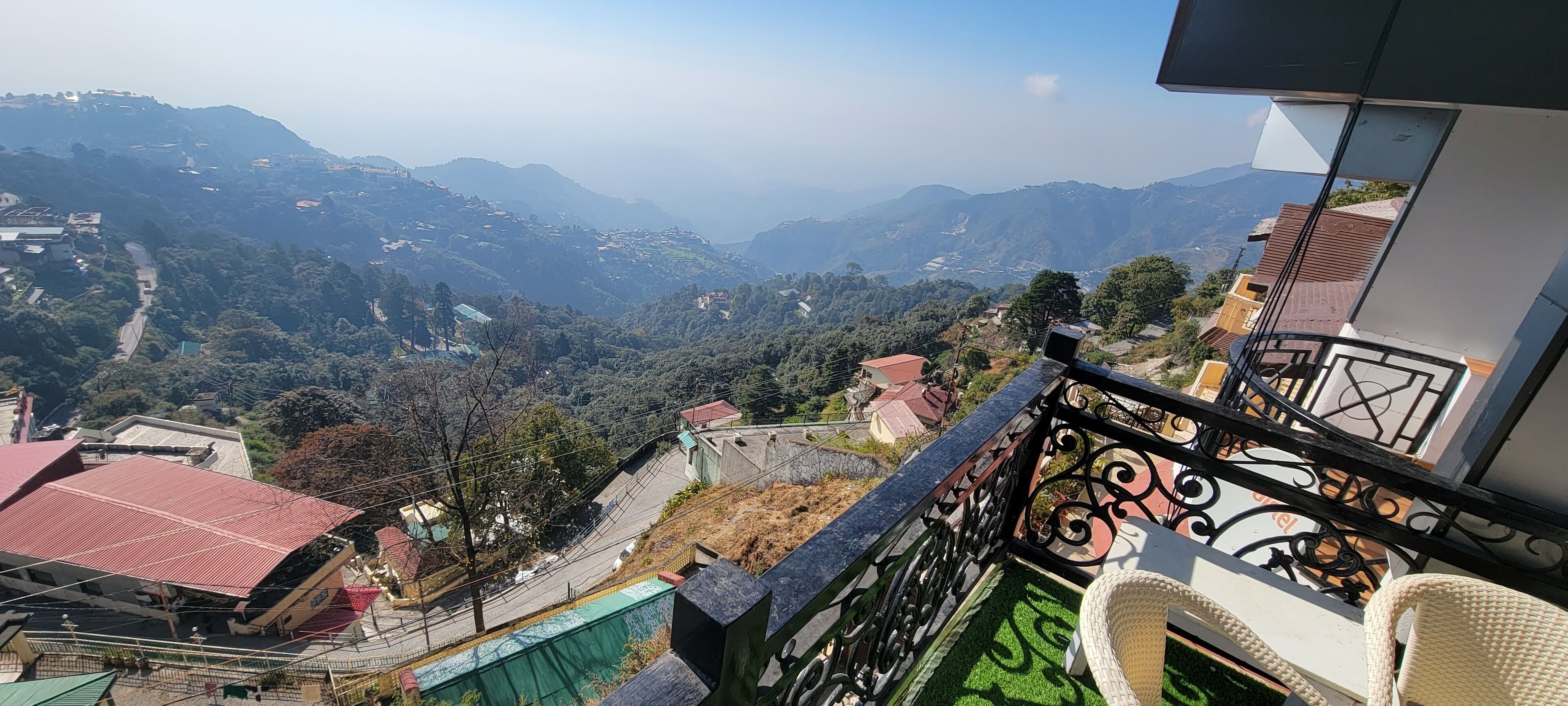 Un balcon donnant sur un paysage montagneux, une route pavée et des immeubles d’habitation.