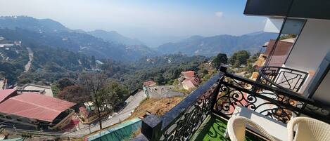 Un balcon donnant sur un paysage montagneux, une route pavée et des immeubles d’habitation.