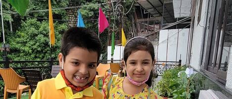 Two children standing next to a potted plant with a variety of flowers.