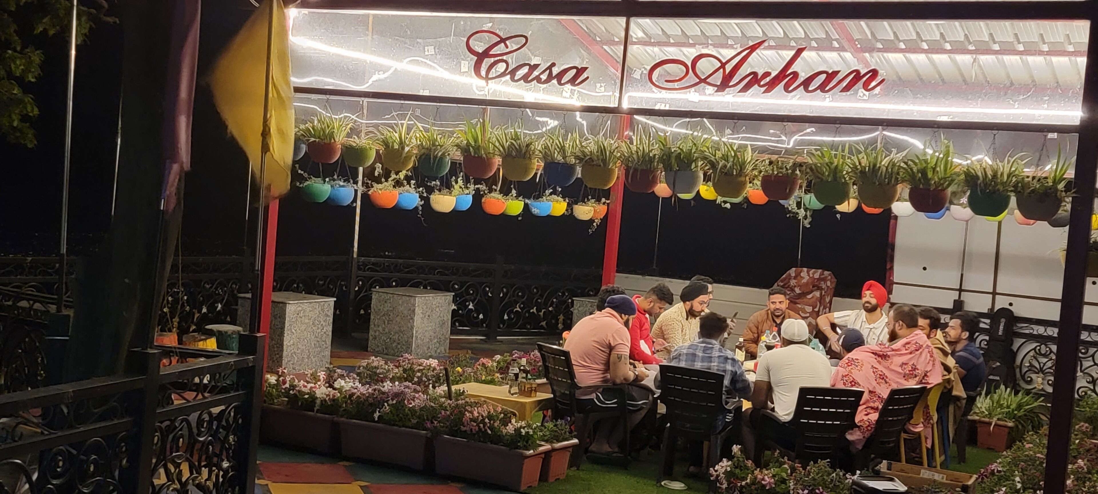 An outdoor seating area with tables and chairs, surrounded by potted plants and flowers.