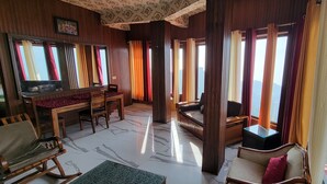 A room with a wooden floor, a dining table, chairs, a sofa, and a TV. - Casa Arhan Luxury Mussoorie Homestay (Dehradun)