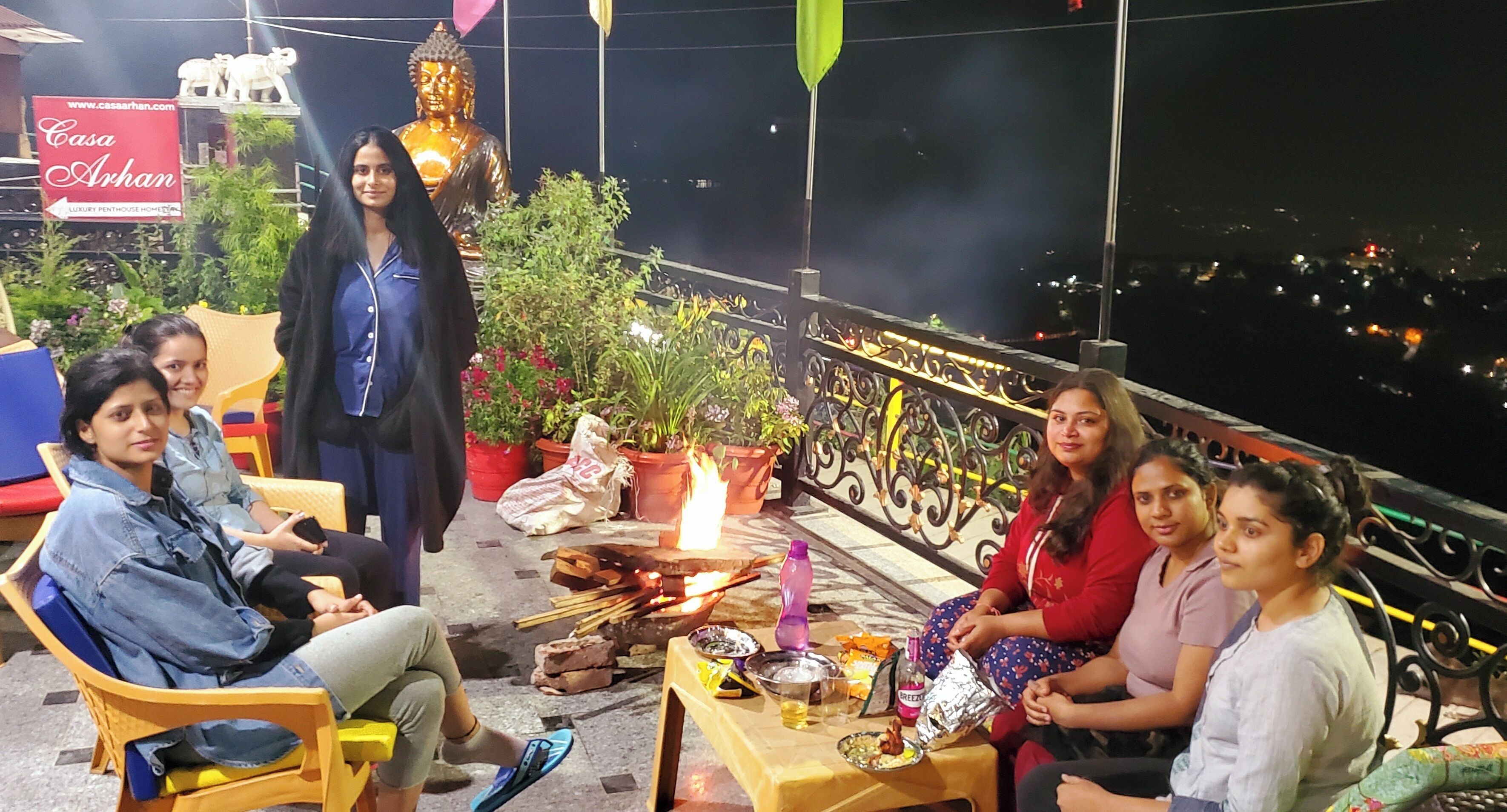 Un grupo de personas sentadas en un balcón con una estatua de Buda, plantas en macetas y un letrero que dice Casa Arhan.