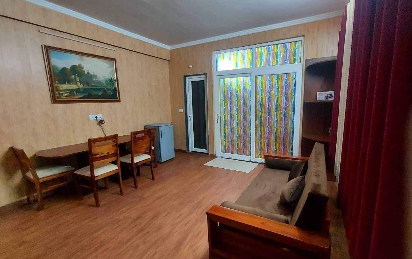 Uma sala de estar com piso de madeira, uma mesa de jantar com cadeiras, um sofá, uma televisão pequena e um quadro na parede.
