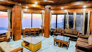 A wooden interior with a dining area, sofas, and large windows. - Casa Arhan Luxury Mussoorie Homestay (Dehradun)