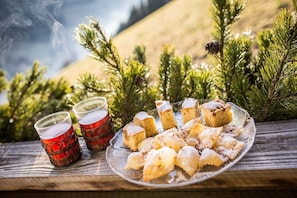 A plate of pastries and two glasses of red beverage on a wooden surface with pine branches in the background.