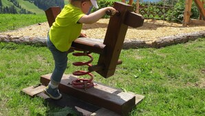 Un bambino gioca su un'altalena di legno in un'area erbosa all'aperto, con montagne sullo sfondo.