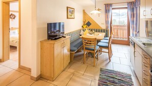 Un ambiente compatto con angolo cottura, zona pranzo con tavolo e sedie, divano, televisione e finestra con tende.