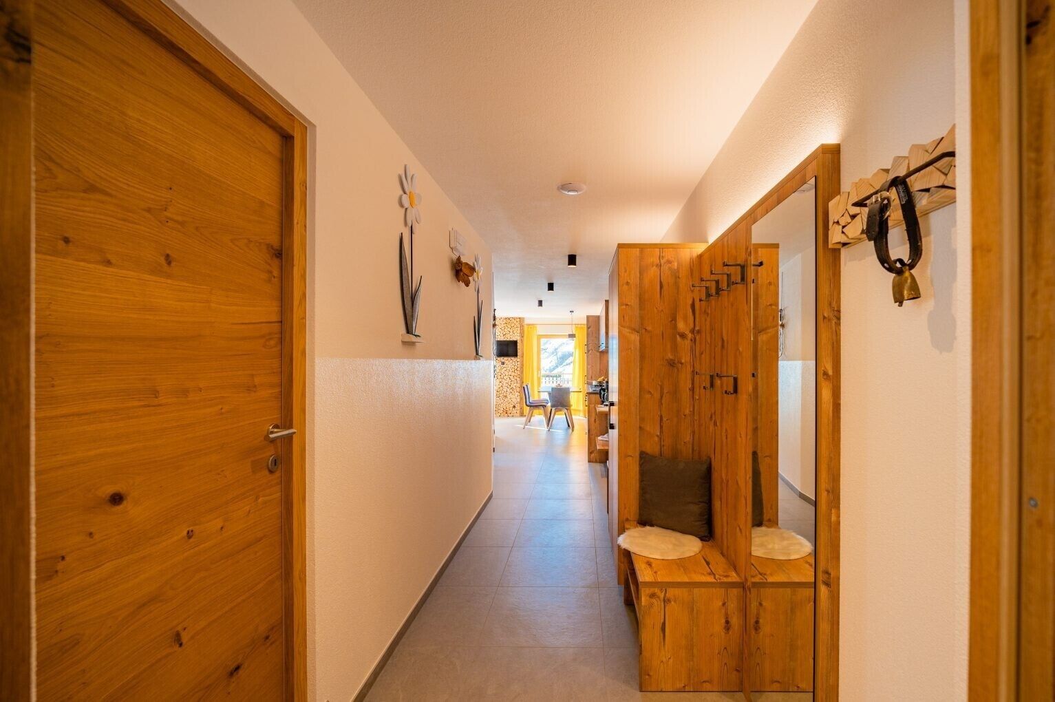 A hallway with wooden doors, a bench, and a view into a room with a window.