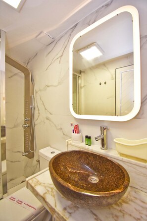 Een badkamer met een marmeren wand, een rond wasbak, een moderne spiegel en een douchecabine.
