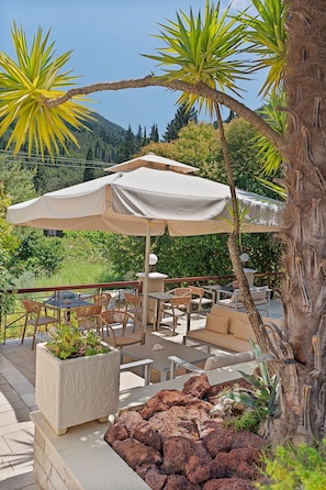 Een terras buiten met een tafel, stoelen, een grote parasol en een rotstuin.