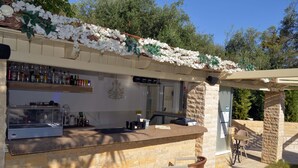 An outdoor bar area with a stone counter, bar stools, and a display case. - Doliva Studio Apartment with Private Pool, Mountain View, Wi-Fi, and Air Conditioning (Corfu)