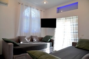 Een moderne kamer met een bank, een bed, een flatscreen televisie en een raam met gordijnen.