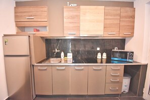 A modern kitchen with wooden cabinets, a refrigerator, a microwave, and a sink. - Doliva Studio Apartment with Private Pool, Mountain View, Wi-Fi, and Air Conditioning (Corfu)